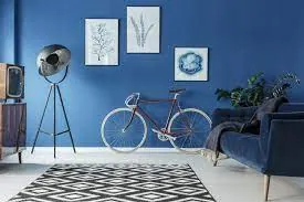 Sala con pared azul intenso, cuadros enmarcados, bicicleta colgada y sofá azul oscuro