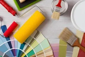 Rodillo, brochas, lata de pintura y carta de colores sobre una mesa de madera