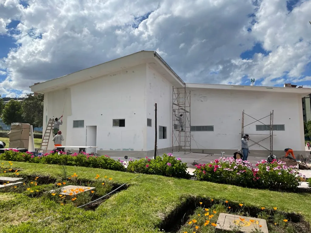 Pintores en andamios y escaleras pintando de blanco las paredes y el alero de una casa de un piso con jardín