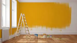 Pared interior a medio pintar de amarillo, con escalera y baldes de pintura