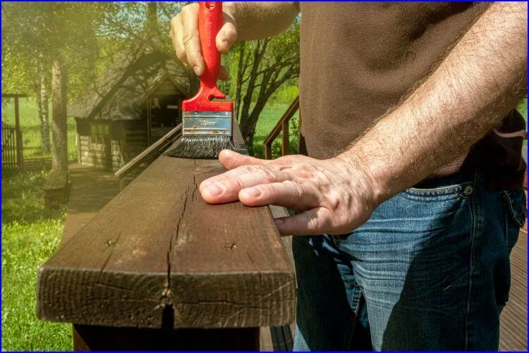 Brocha aplicando barniz sobre una baranda de madera al aire libre